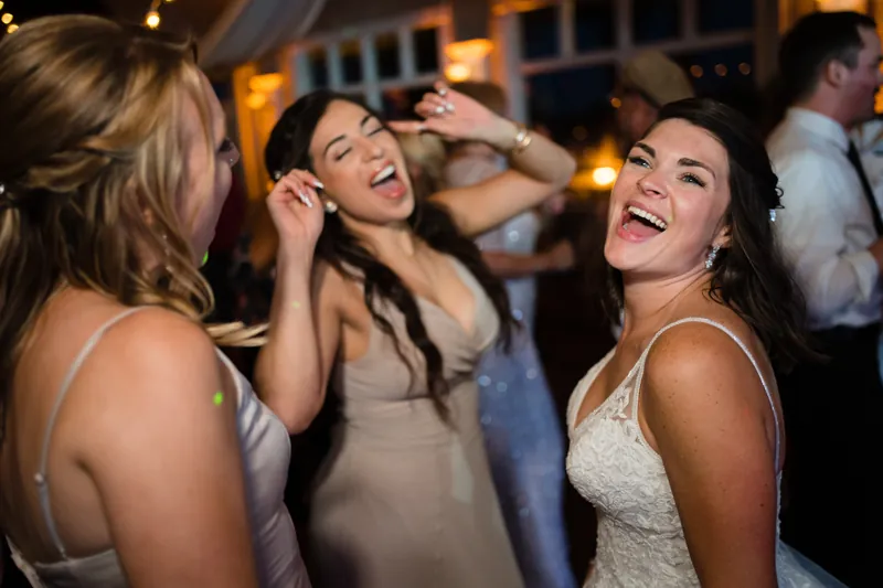 Three women dance together at the reception, grinning and enjoying the evening at The White Room.