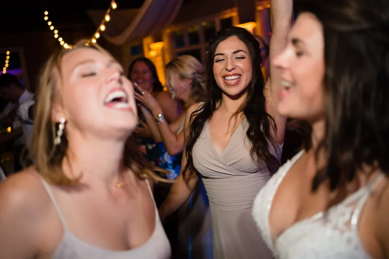 Guests laugh and dance together at The White Room reception, bathed in warm overhead string lights.