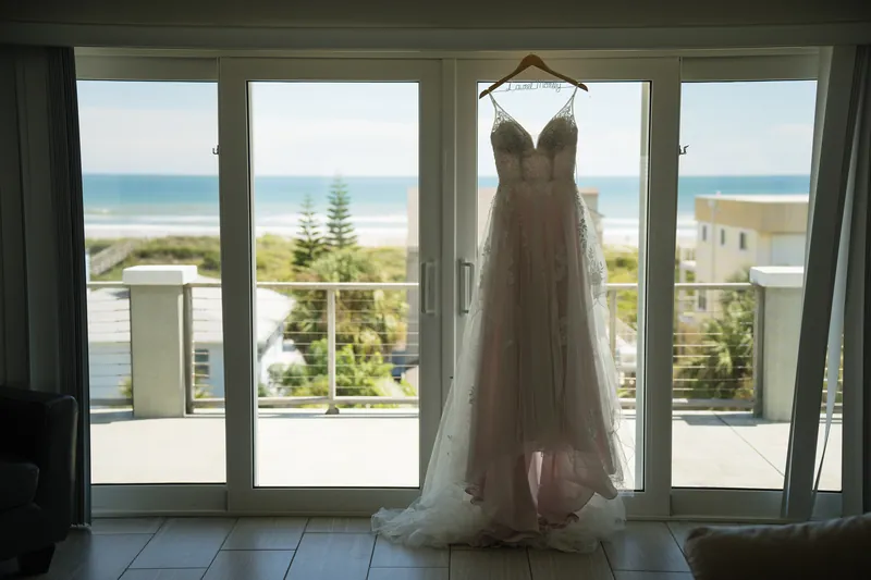 Laurel's wedding dress hangs before floor-to-ceiling windows with ocean views at The White Room.