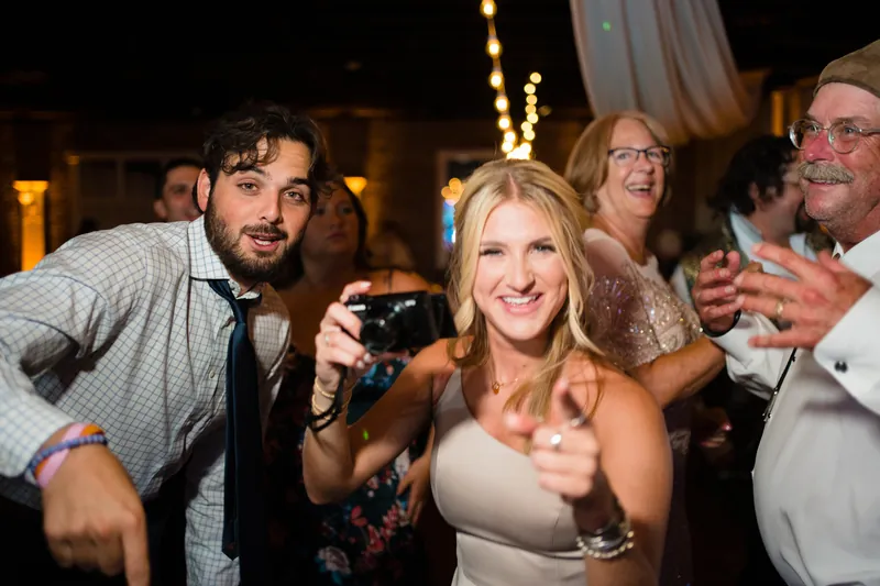 A guest holds up a phone to capture the moment while dancing surrounded by friends at the reception.