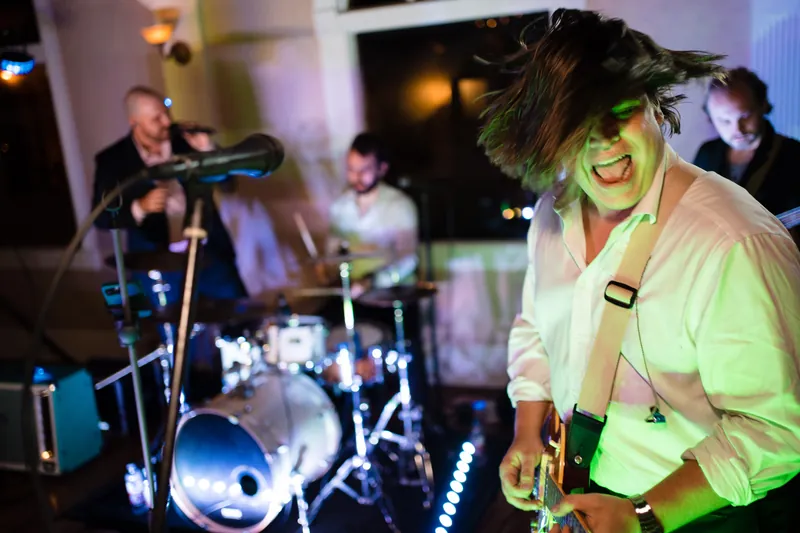 A guest in a neon yellow shirt dances enthusiastically while the band plays on stage.