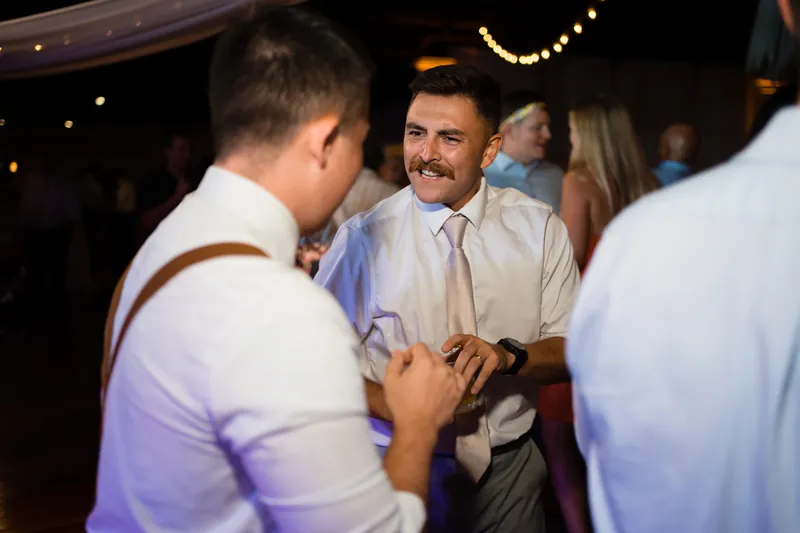 Jake in a tan vest and white shirt shares a laugh with guests on the dance floor.