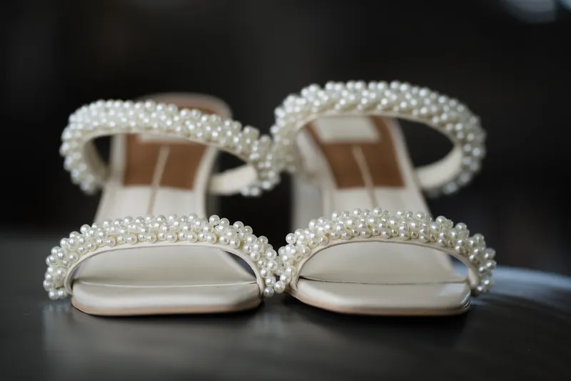 Pearl-encrusted white bridal heels sit side by side on a dark surface before the ceremony.