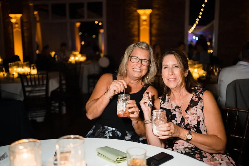 Two women clink glasses at a candlelit table during the reception.