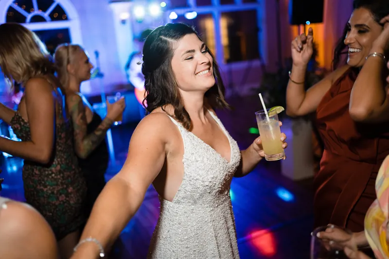 Laurel dances under blue lighting, holding a cocktail surrounded by guests at the reception.
