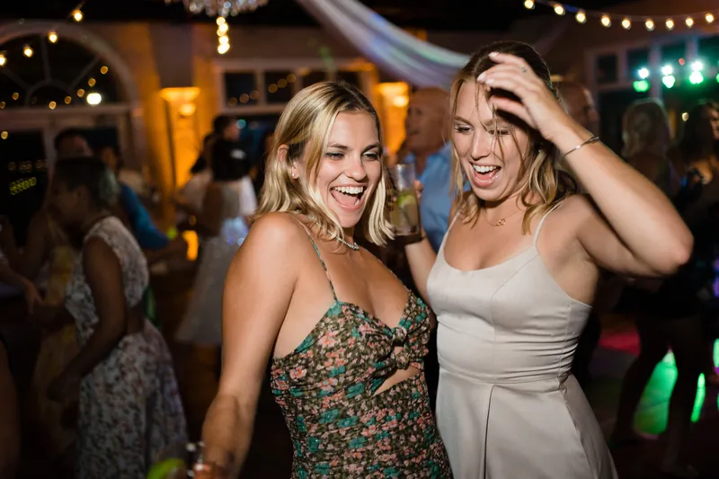 Two women smile together on the dance floor with festive lighting behind them.