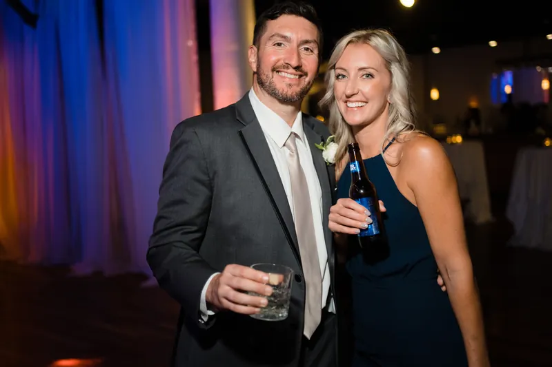Jake and a guest clink glasses, both grinning at the reception celebration.