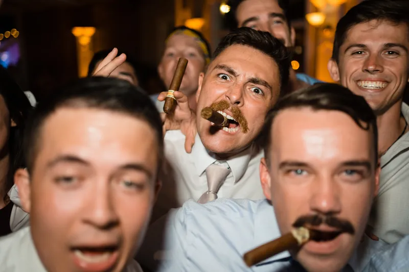 Jake and guests in white shirts laugh while smoking cigars at The White Room's reception.