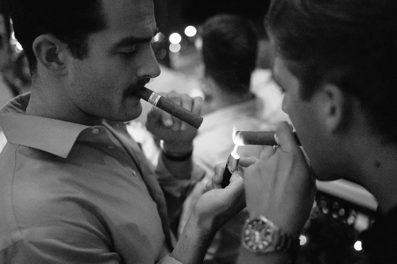 Two men in light-colored shirts enjoy cigars together in black and white.