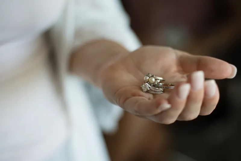 Laurel's hand displays a diamond engagement ring and wedding band against white fabric.