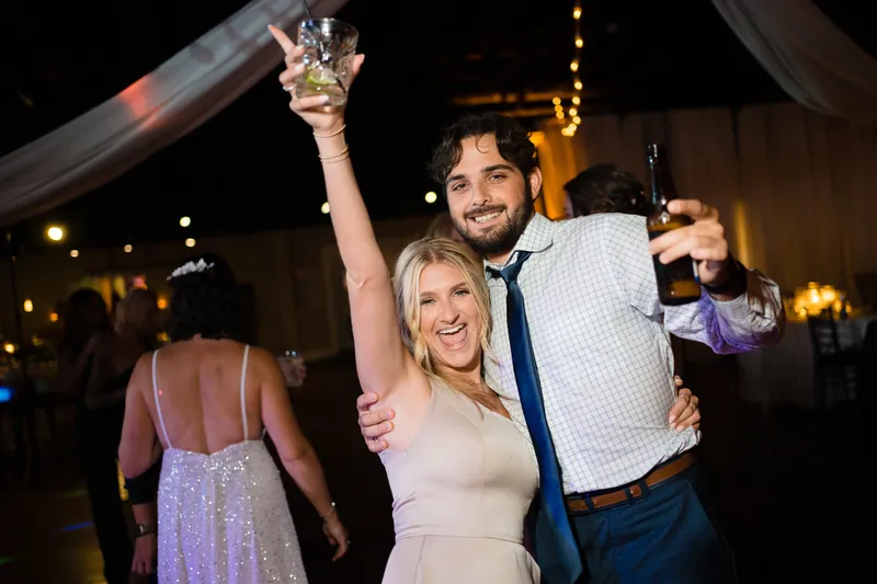 Laurel holds a champagne glass aloft while Jake stands beside her at the celebration.