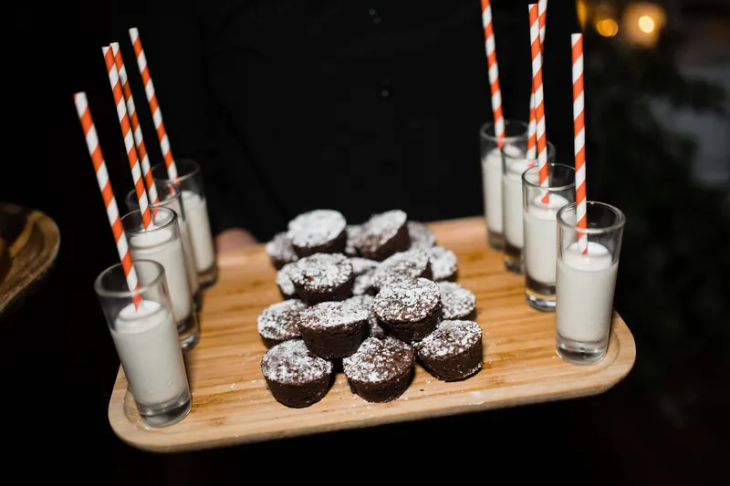 Chocolate cupcakes with striped candles and milk glasses arranged on a wooden board.