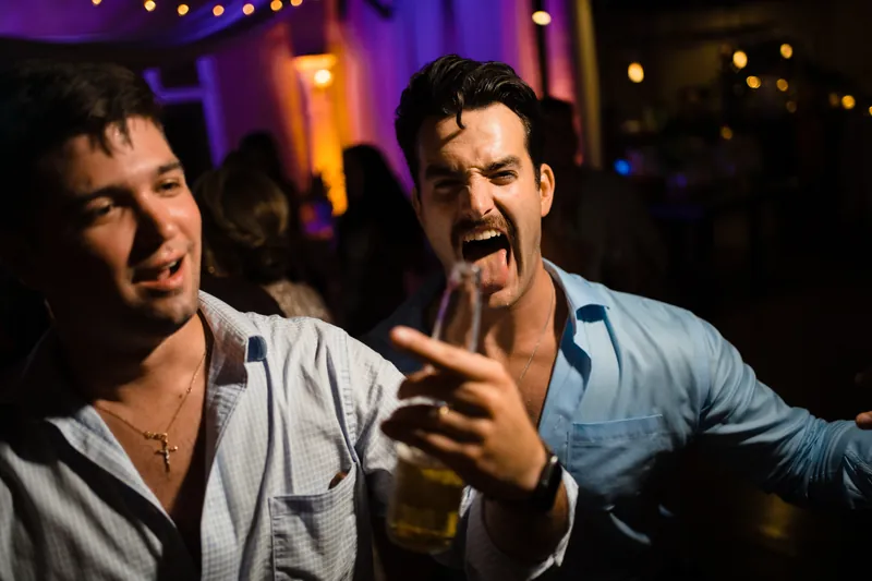 Two male guests in light blue shirts smile and gesture animatedly while enjoying the reception celebration.