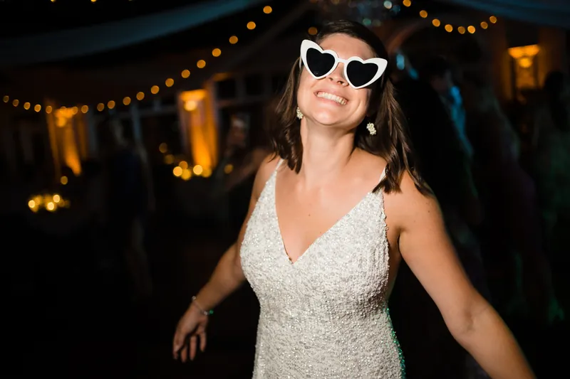 Laurel wears a beaded white gown and heart-shaped sunglasses while dancing under golden string lights at The White Room.