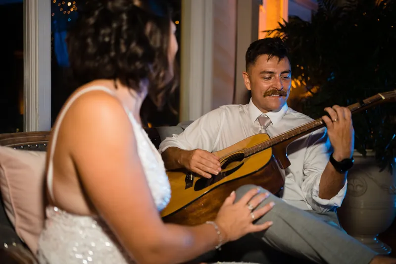 Jake plays guitar for Laurel, who sits facing him in her beaded wedding dress during an intimate moment.