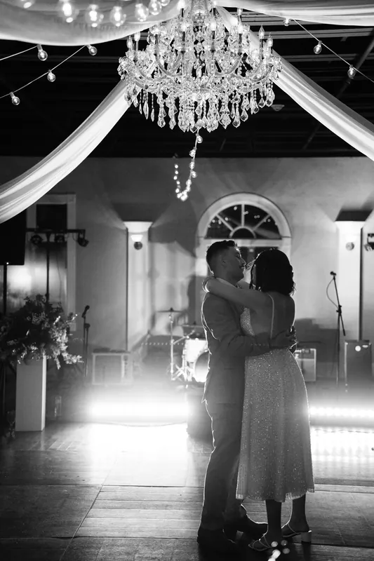 Laurel and Jake embrace under a crystal chandelier in a black and white shot at The White Room.