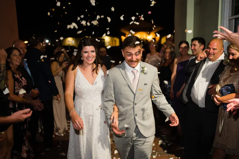 Laurel and Jake walk hand-in-hand down an outdoor aisle at The White Room as guests toss gold confetti around them.