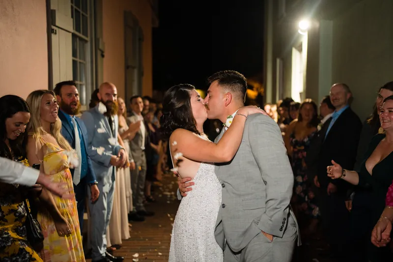 Laurel and Jake kiss on a brick pathway at The White Room while guests watch and applaud on either side.