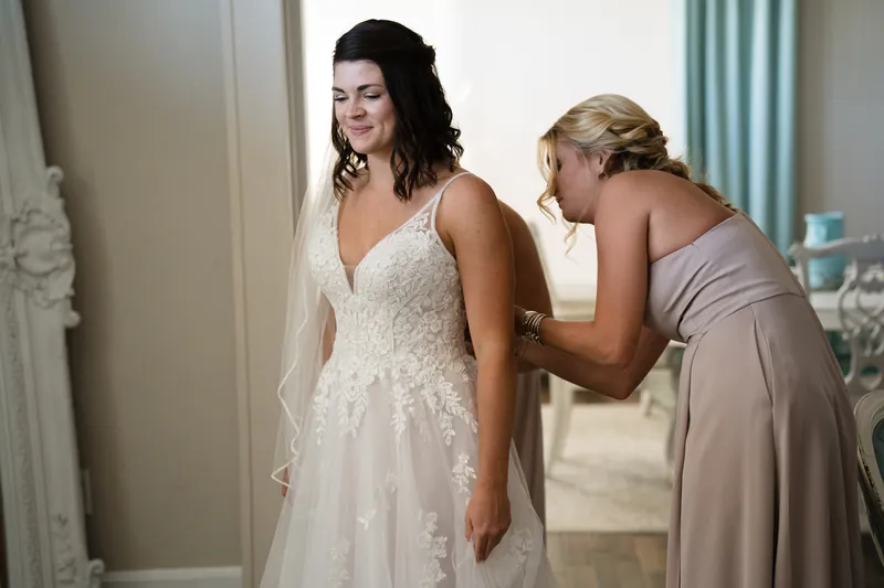 A woman helps adjust Laurel's flowing white gown in the bridal suite.