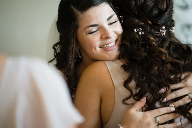 A guest hugs Laurel warmly, both smiling with eyes closed during the getting-ready moments.