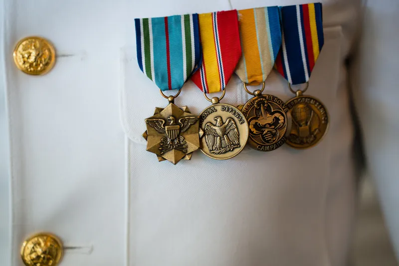 Military service medals hang from colorful ribbons pinned to white dress uniform fabric with gold buttons.
