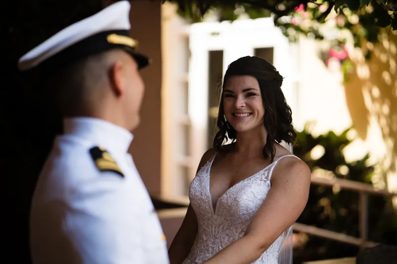 Jake in a white naval uniform smiles at Laurel, who wears a beaded white gown with a plunging neckline at The White Room.