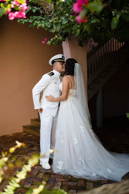 Jake and Laurel kiss beneath magenta bougainvillea, her veil trailing across the brick courtyard.