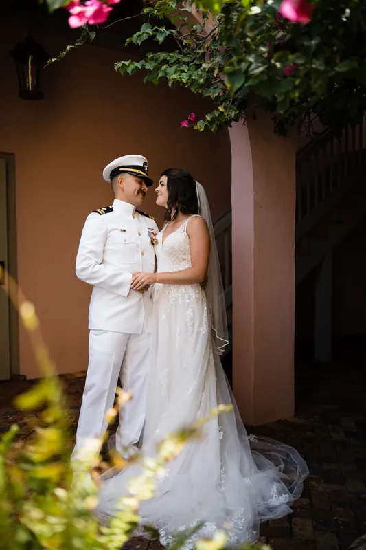 Jake and Laurel embrace under blooming flowers framed by the terracotta building.