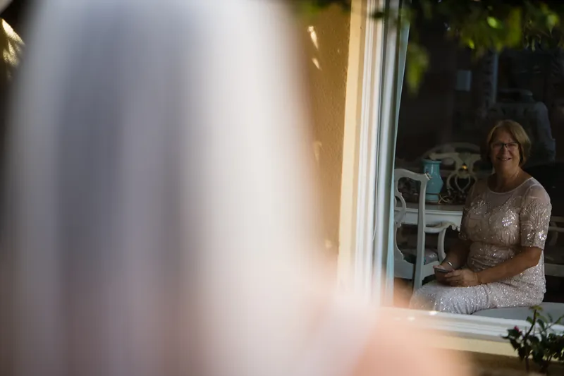 Laurel sits by a window in her beaded dress, gazing toward the camera.