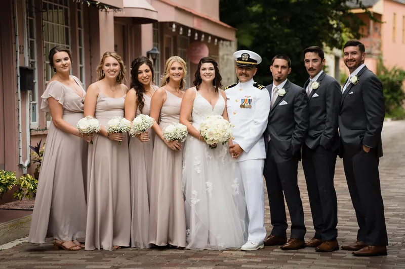 Laurel and Jake stand with their wedding party holding bouquets outside The White Room's terracotta facade.