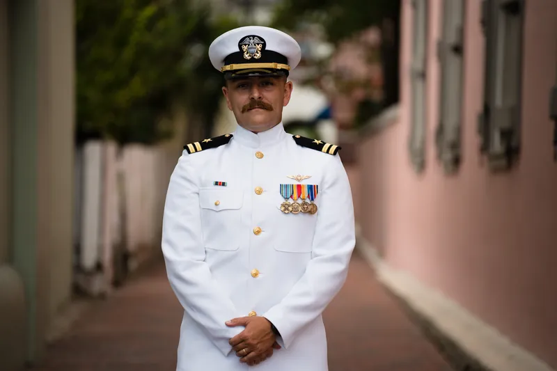 Jake stands alone in full naval dress whites with medals and insignia, facing the camera in The White Room's courtyard.