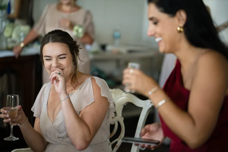 Laurel laughs with champagne in hand while conversing with a guest in a burgundy dress at The White Room.