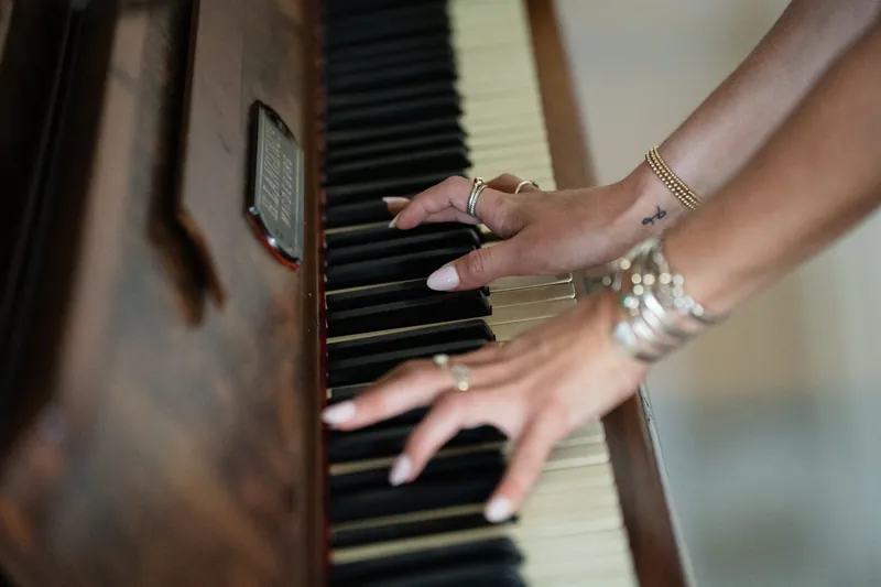 Manicured hands with pearl bracelets play piano keys during an indoor reception moment.
