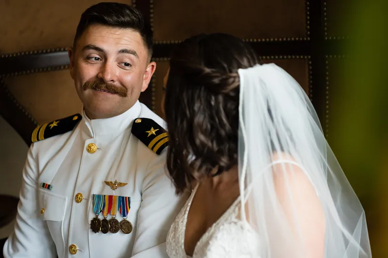 Jake in white naval dress uniform smiles as Laurel leans toward him, her veil visible over his shoulder.