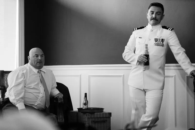 Two men in formal attire stand in conversation at The White Room, one wearing a white naval uniform with medals.