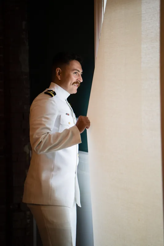 Jake stands in profile at The White Room wearing a cream-colored suit jacket, adjusting his collar with a focused expression.