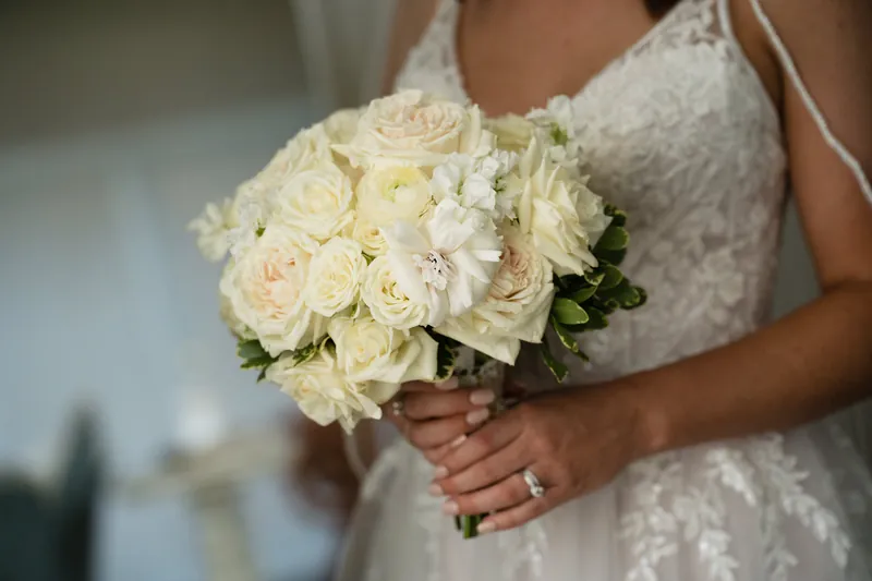 Laurel holds a cream and white rose bouquet with greenery, visible from the torso down in her beaded wedding dress.