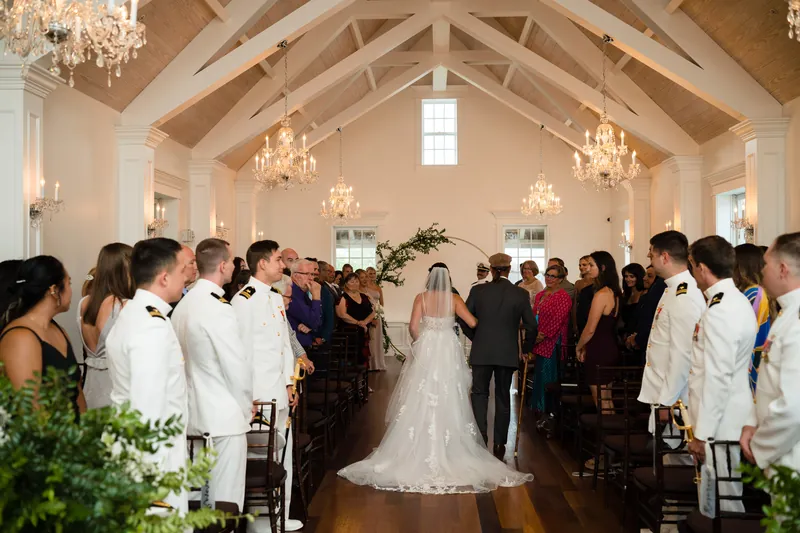 Laurel stands at the altar in her beaded gown as guests gather around the vaulted White Room sanctuary during the ceremony.