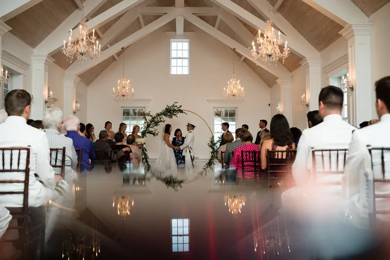 Guests seated in rows watch the couple exchange vows under chandeliers in the bright, modern venue.