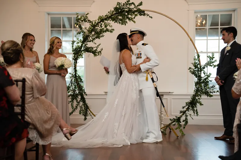 Laurel and Jake exchange vows beneath a greenery-draped arch as guests look on.