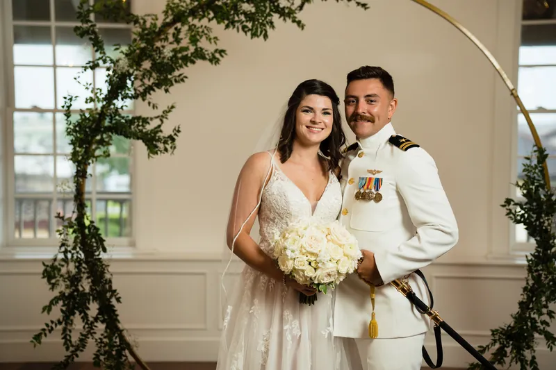 Laurel smiles beside Jake in his naval uniform under the flower-framed arch at The White Room.