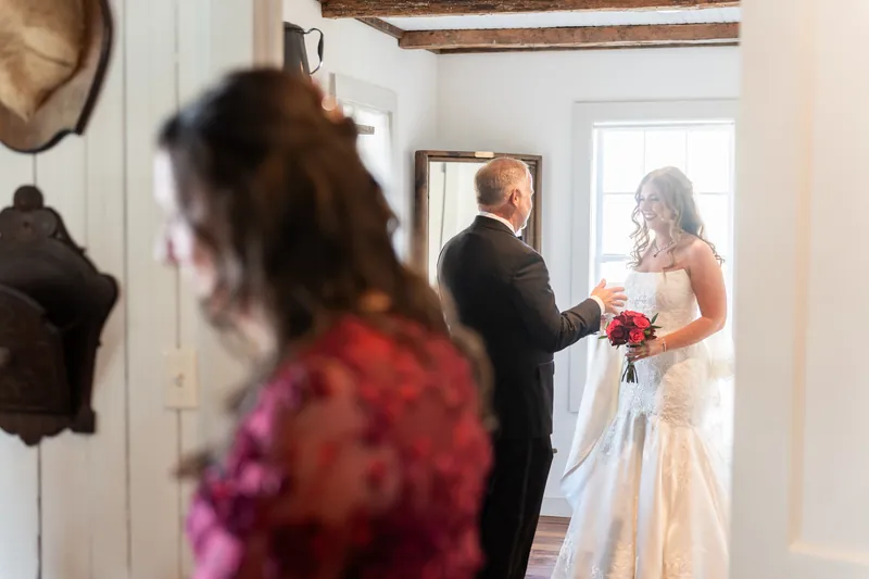 Kevin greets Lauren in the chapel entryway as guests watch, both holding her red flowers.