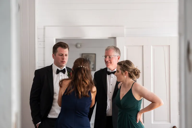Wedding guests in formal wear chat in a bright hallway before the ceremony begins.