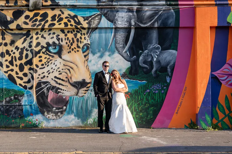Lauren and Kevin pose in front of a vibrant mural featuring a leopard and colorful abstract designs.