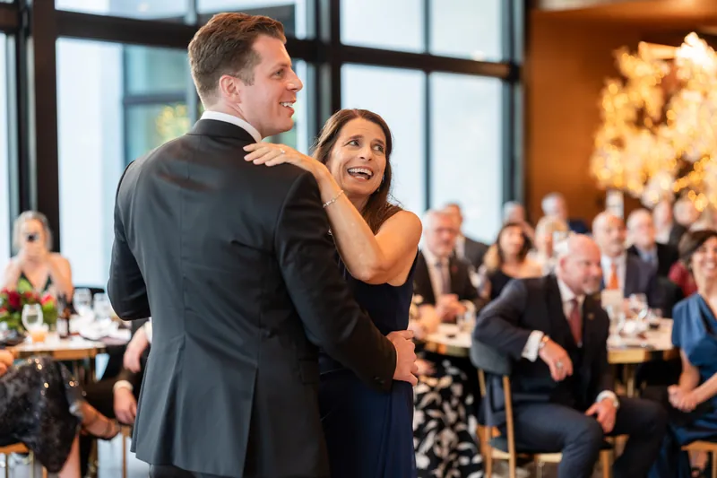 Kevin and a guest laugh together during a dance, surrounded by seated attendees in the softly lit reception space.