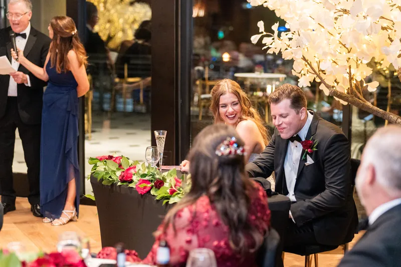 Kevin laughs while greeting guests near the glowing trees and pink floral arrangements at their celebration.