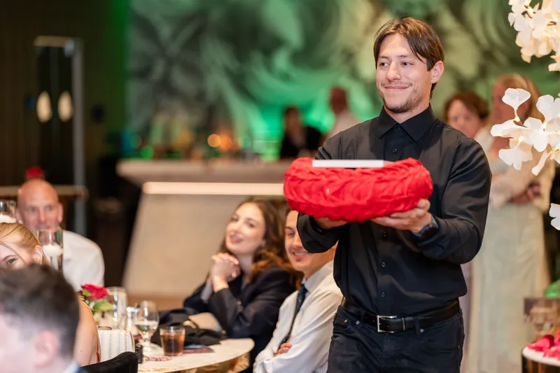 A guest presents a red rose arrangement to the couple during the reception festivities.