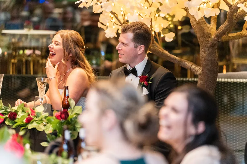 Lauren beams at Kevin as they sit together at their sweetheart table surrounded by guests and illuminated florals.