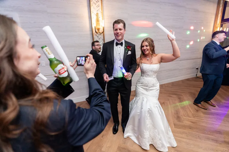 Lauren in her white gown and Kevin in his tuxedo raise champagne glasses as guests celebrate around them.