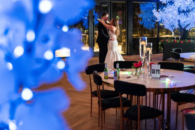 Lauren and Kevin share a dance as blue uplighting and festive décor frame the venue.